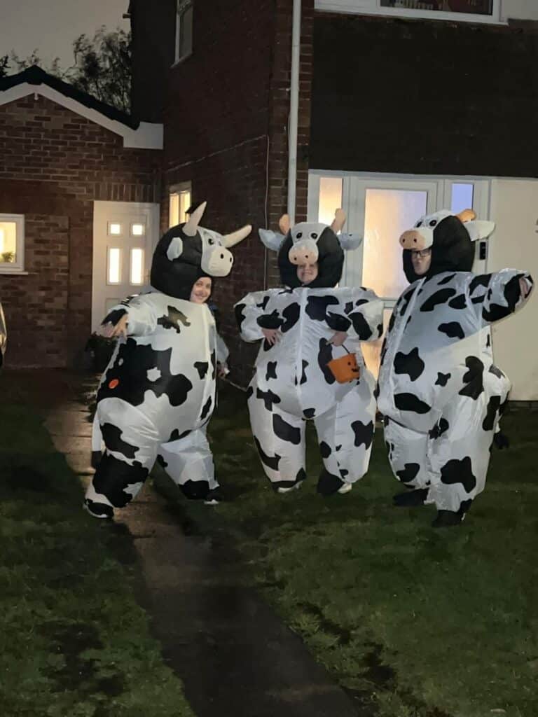 Three women stand in front of a house in giant inflatable cow costumes as they prepare to go trick or treating!